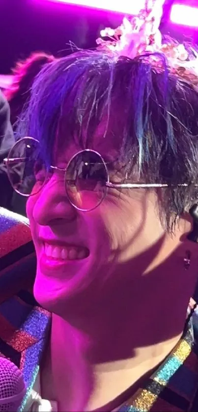 Smiling musician with round glasses under vibrant purple lighting.