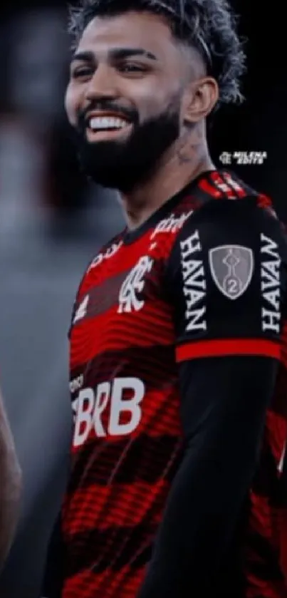 Soccer player in red and black jersey smiling on field.