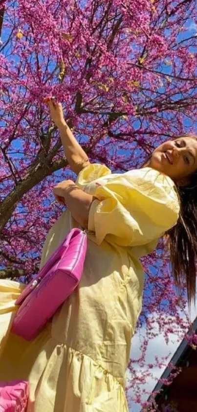 Woman in yellow dress under vibrant pink tree.