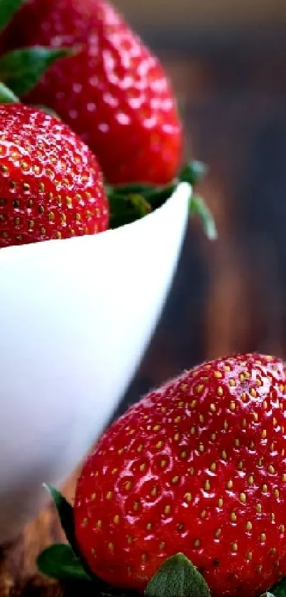 Red strawberries in a white bowl, placed on a wooden surface.