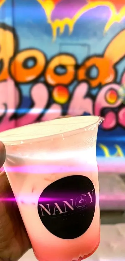 Hand holds drink against vibrant graffiti background.