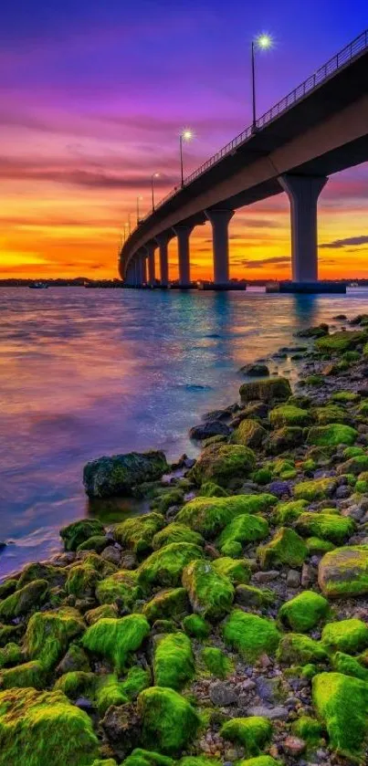 Vibrant sunset over a bridge with colorful sky and green mossy rocks.