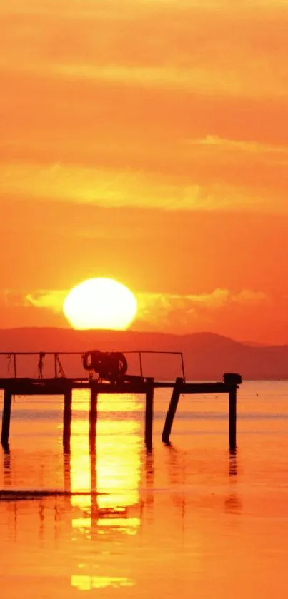 Fiery orange sunset over a serene pier reflecting on calm water.