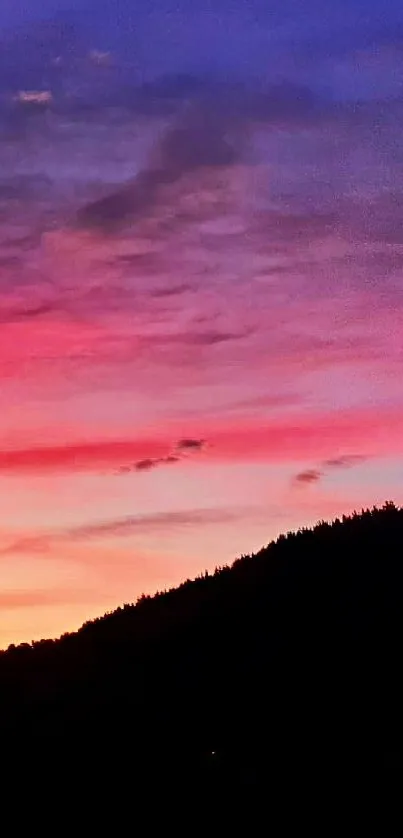 Vibrant sunset sky with pink, purple, and orange hues over mountain silhouette.