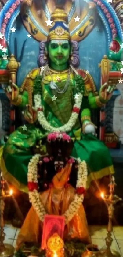 Colorful Hindu deity in a temple setting, adorned with flowers and oil lamps.