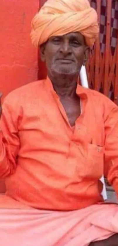 Man in vibrant orange traditional attire with orange turban seated.