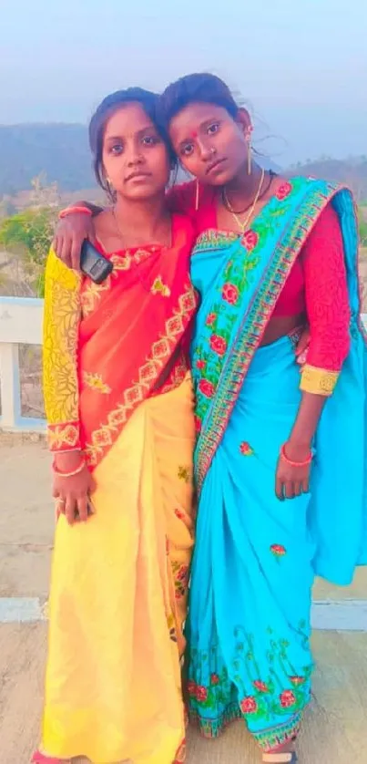 Two women in colorful sarees with a scenic background.