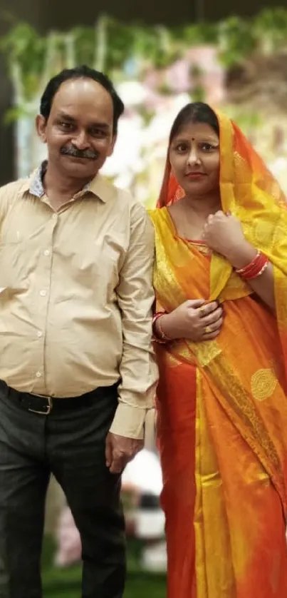 Couple in vibrant traditional attire with decorative background.