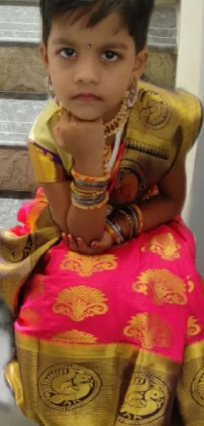 Young girl in a vibrant traditional pink dress, sitting on steps.