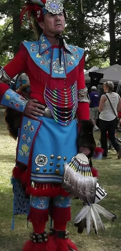 Man in vibrant red and blue traditional attire with feathers and accessories.