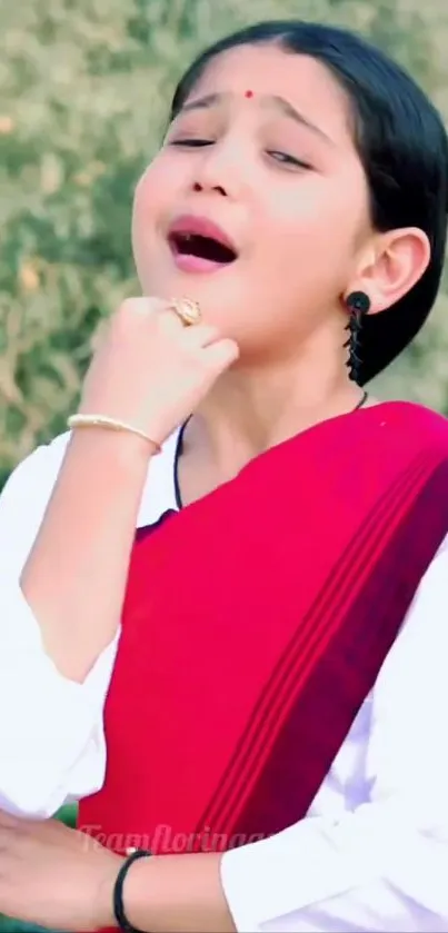 Child in vibrant traditional red attire singing.