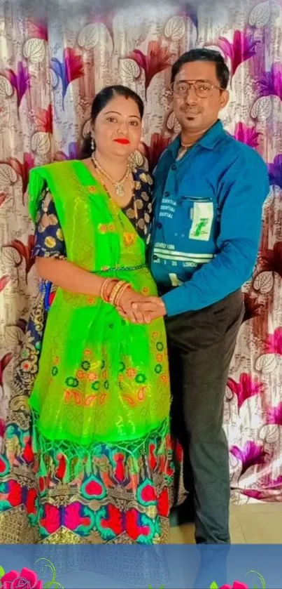 Traditional couple in vibrant attire with floral backdrop.