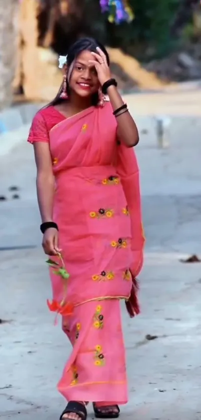 Young woman in vibrant pink saree with floral designs on a street path.