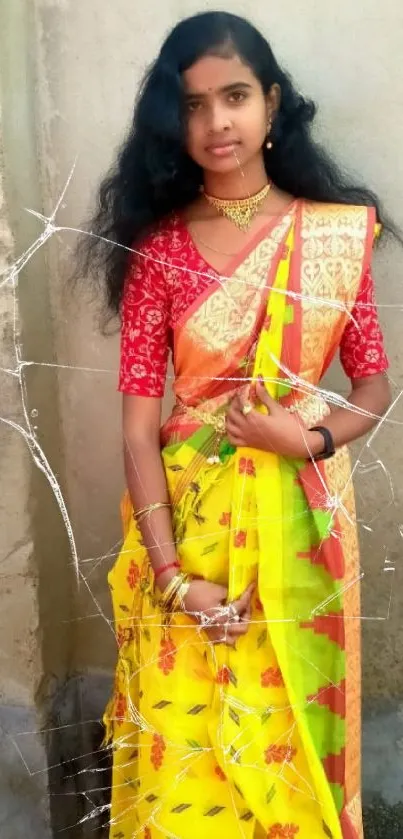 Woman in vibrant yellow and red traditional saree against a neutral wall backdrop.