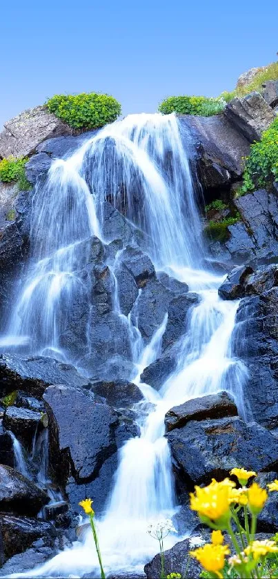 Vibrant waterfall with lush greenery and yellow flowers under a clear blue sky.