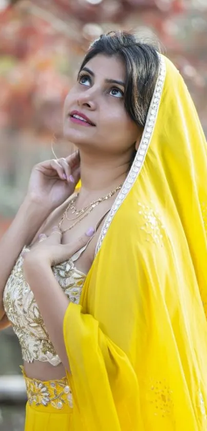 Woman in vibrant yellow attire with autumn foliage background.