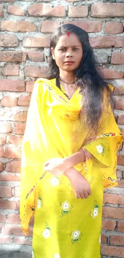 Woman in vibrant yellow dress against rustic brick wall.