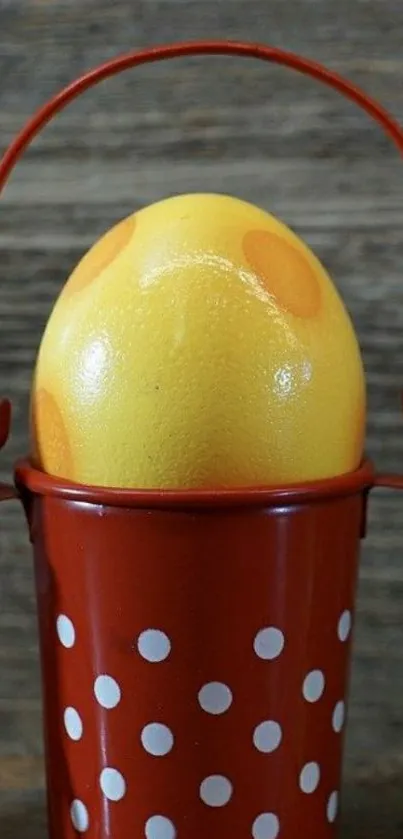 Yellow egg with orange spots in red polka dot bucket on wood.