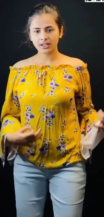 Woman in vibrant yellow floral blouse against a dark background.