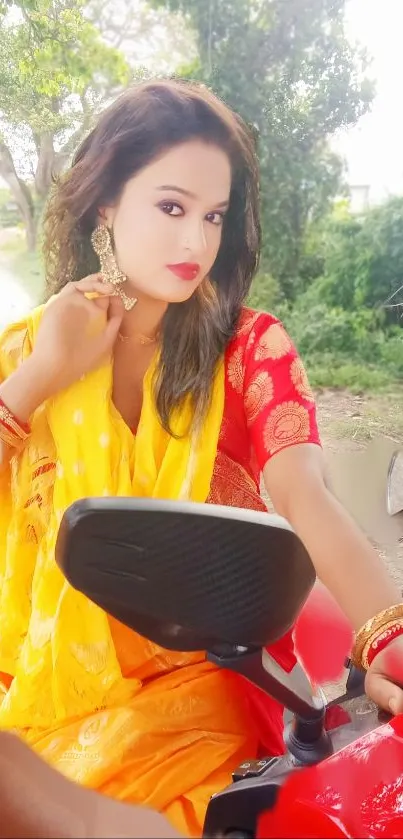 Woman in a vibrant yellow saree sitting on a red motorcycle, outdoor background.