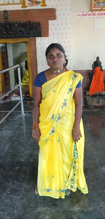 Woman in a vibrant yellow sari standing inside a temple with traditional decor.