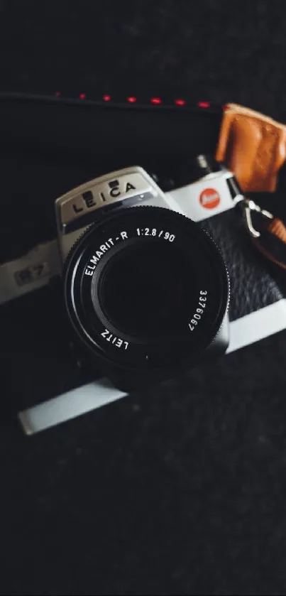 A Leica vintage camera with a leather strap, set against a dark surface.