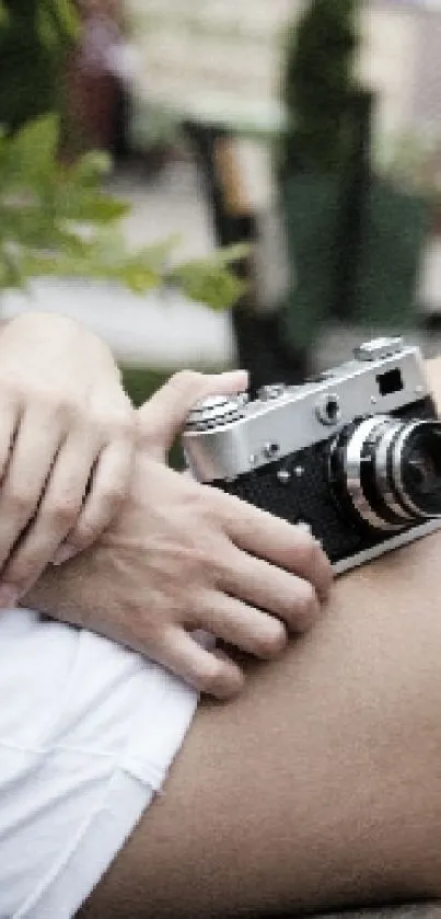 Woman holding vintage camera sitting on bench.