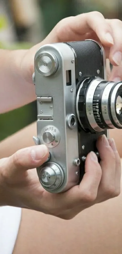 Hands holding vintage camera in soft focus wallpaper.