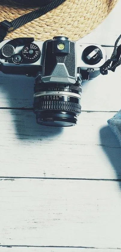 A vintage camera on a wooden table with a hat and denim accents.