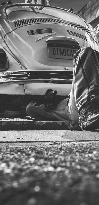 Mechanic working under a vintage car in a black and white garage scene.