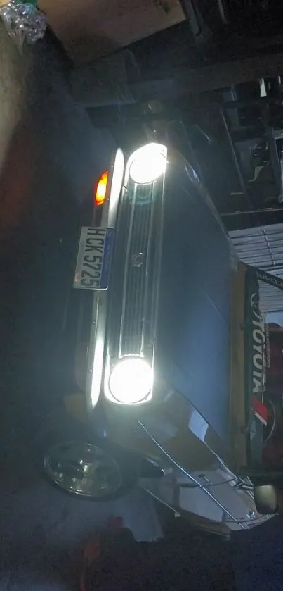 Dark vintage car in a garage setting with headlights on.