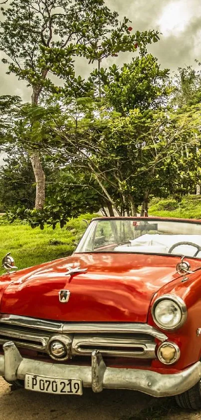 Vintage red car on a scenic countryside road amidst lush greenery and a cloudy sky.