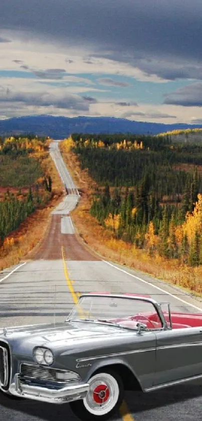 Vintage car on scenic road with autumn trees under a cloudy sky.