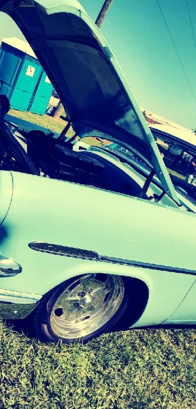 Sky blue vintage car with hood open under sunny sky.