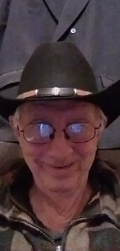 Smiling person wearing a cowboy hat and glasses with a rustic background.