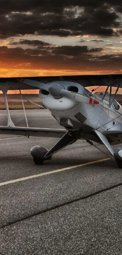 Vintage biplane on runway at sunset with vibrant sky.