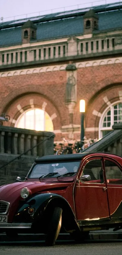 Vintage red car parked by a historic building at dusk.