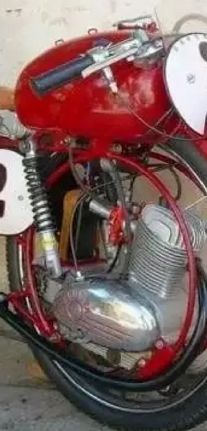 Vintage red motorcycle with race number two, parked by a beige wall.