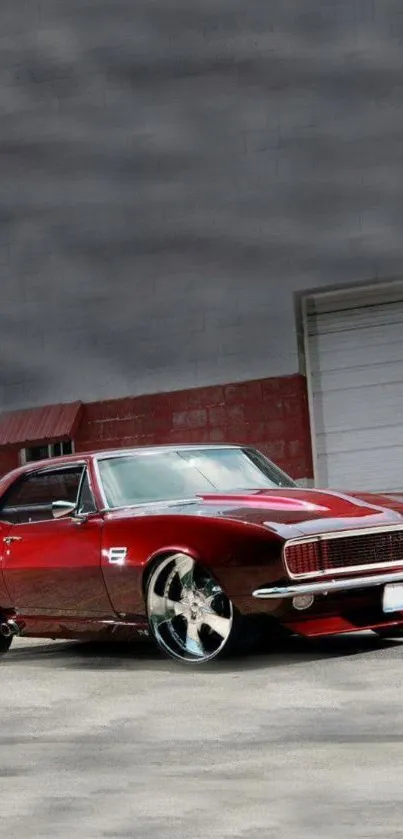 Vintage red muscle car parked outside a garage with chrome wheels.