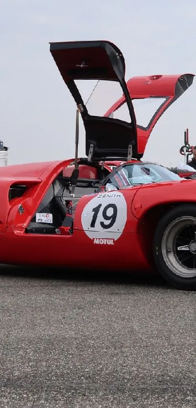 Vintage red sports car at a motorsport event with open doors.