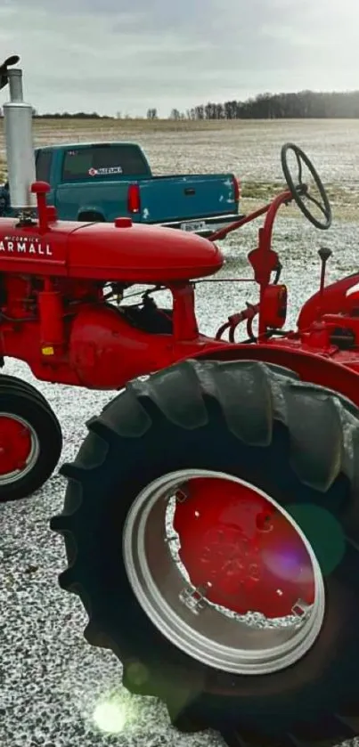 Vintage red tractor in a snowy field with a blue truck.