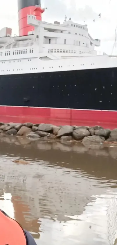 Vintage ship reflecting on calm water with a rocky shoreline.