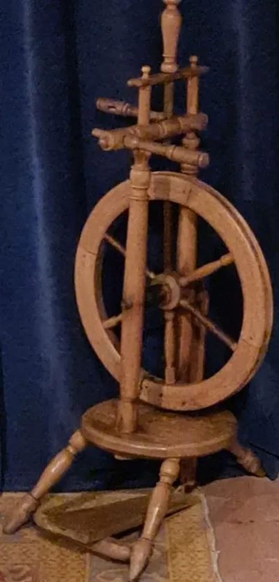 Vintage wooden spinning wheel against a blue curtain.