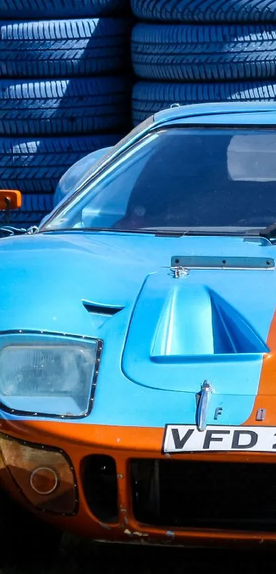 Blue and orange vintage sports car in front of stacked colored tires.