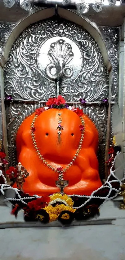 Bright orange Ganesh idol in temple alcove with ornate decor.