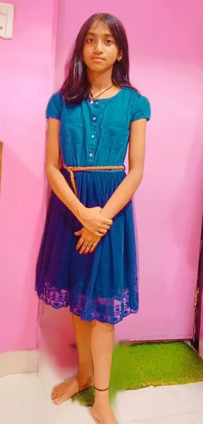 Young girl standing in a vibrant pink room wearing a stylish blue dress.