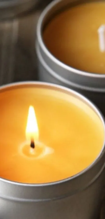 Close-up of a lit candle in a silver tin, emanating a warm amber glow.