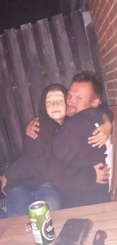 Family hugging at night, against a wooden fence and brick wall.