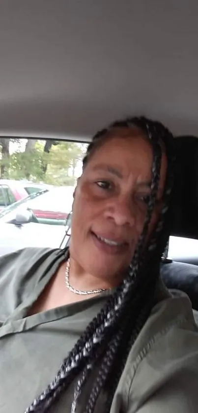 Smiling person with braided hair in car interior.