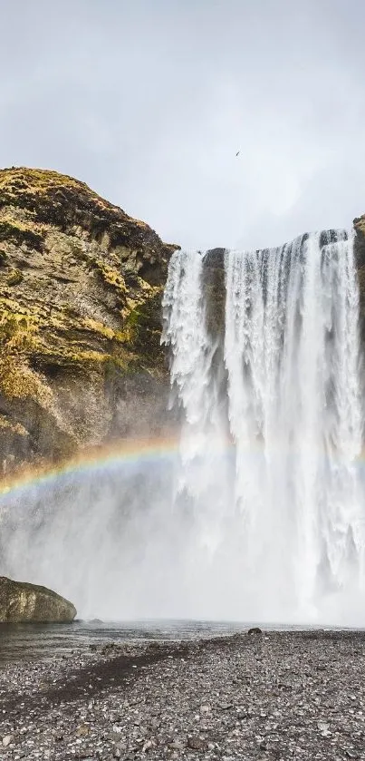 Majestic waterfall with rainbow and misty surroundings.